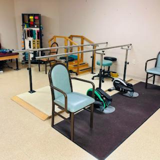 A rehabilitation therapy room equipped with exercise equipment and chairs for patient use.