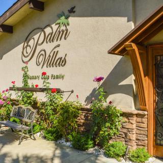 Front view of a building with the sign 'Palm Villas', surrounded by a garden with flowers and plants.