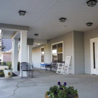 A building with a spacious porch featuring chairs and decorative columns.