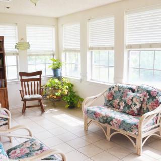 A bright sunroom filled with natural light, featuring rattan furniture and indoor plants.