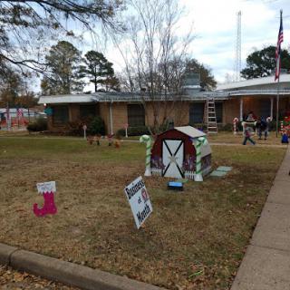 A festive front yard decorated for the Christmas season, featuring colorful signs and a decorative doghouse.