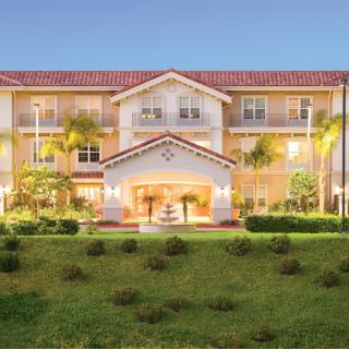 A well-lit residential building with manicured landscaping and palm trees.