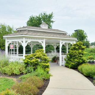 A charming white gazebo surrounded by lush greenery and a curved pathway in a garden setting.