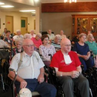 A group of elderly people gathered indoors for a meeting.