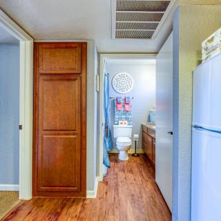 A hallway leading to a bathroom with wood flooring and adjacent kitchen area.