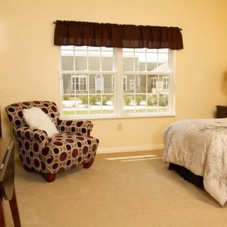 A cozy bedroom with a patterned armchair, bed, and large window.
