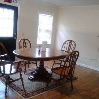 A cozy dining room with a round wooden table and chairs, featuring natural light from a nearby window.