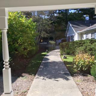 A pathway leading through a garden area towards a house, surrounded by trees and shrubbery.