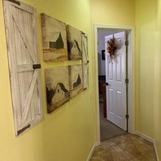 A cozy hallway with yellow walls, featuring decorative barn-themed art and wooden shutter accents, leading to an open door.