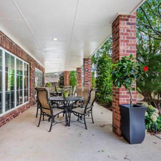 An inviting covered patio with a table and chairs surrounded by brick columns and lush greenery.