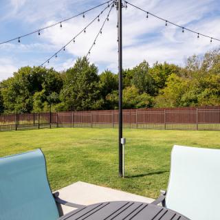 A cozy outdoor patio with string lights, overlooking a grassy lawn and surrounded by trees.