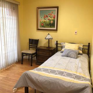 A cozy bedroom with a single bed, yellow walls, and a window with curtains.