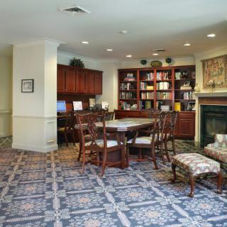A cozy library space with bookshelves, a table, and chairs, featuring a patterned carpet.