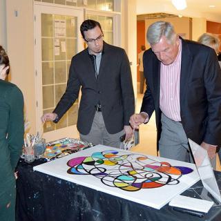 People engaged with a colorful painting at an indoor event.