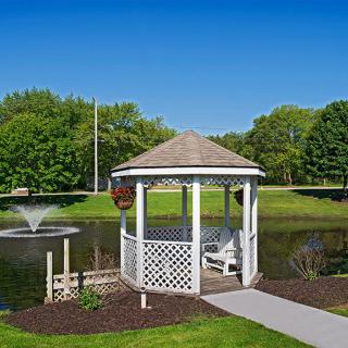 A serene gazebo by a pond with a fountain surrounded by lush greenery.