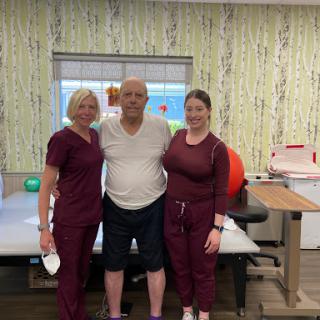 A patient stands with two healthcare professionals in a rehabilitation center, showcasing the supportive environment of physical therapy.