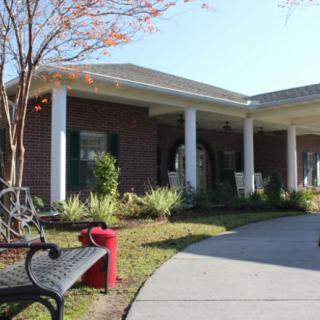 A brick house with a covered porch, surrounded by landscaping and a bench in the foreground.