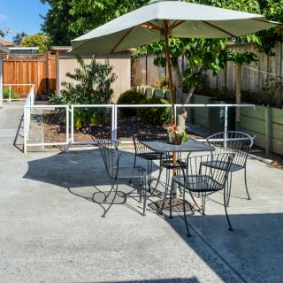 A sunny outdoor patio with a table, chairs, and an umbrella.