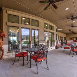 A covered patio with tables and chairs, featuring large windows and ceiling fans.