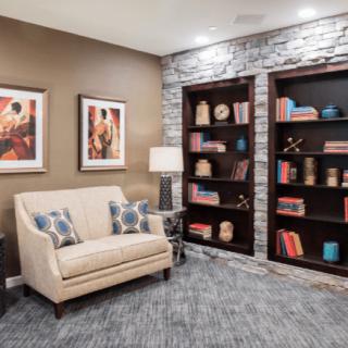 A cozy living room with a beige couch, decorated bookshelves, and framed artwork.