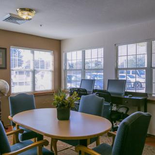 A well-lit meeting room with a conference table, chairs, and computer desks by the windows.