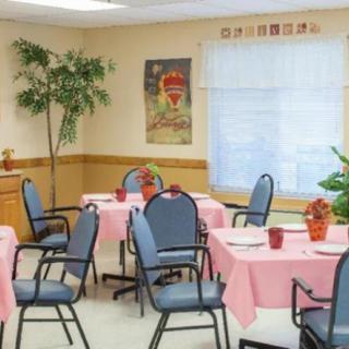 A small dining area with tables covered in pink tablecloths and blue chairs, decorated with plants and wall hangings.