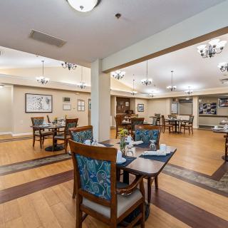 An elegant dining area with neatly arranged tables and chairs, illuminated by chandeliers.