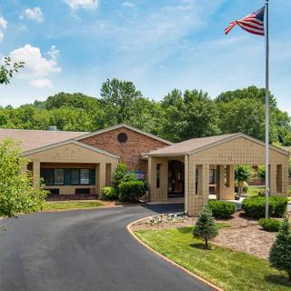 A brick building with a driveway and an American flag in front, surrounded by trees under a blue sky.