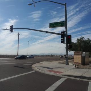 A view of an intersection showing traffic lights and road signs under a cloudy sky.