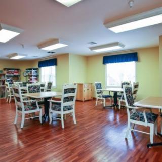 A bright community dining area with several tables and chairs, featuring hardwood floors and large windows.