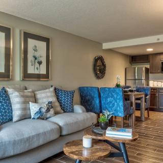 A modern living room with a cozy sofa, colorful cushions, and a stylish coffee table, extending into an open kitchen and dining area.