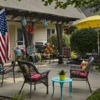 A cozy outdoor patio with seating arrangements, an umbrella for shade, and an American flag displayed.