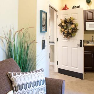 A cozy living space featuring a decorative wreath on the door, with a view into a kitchenette adorned with charming decor.