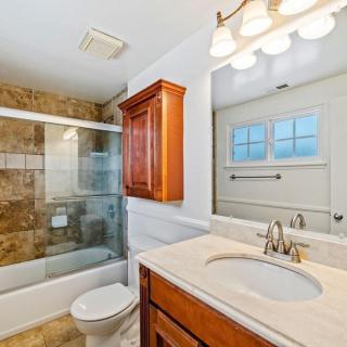 A clean and well-lit bathroom with a sink, wooden cabinet, and a glass-enclosed shower and bathtub.