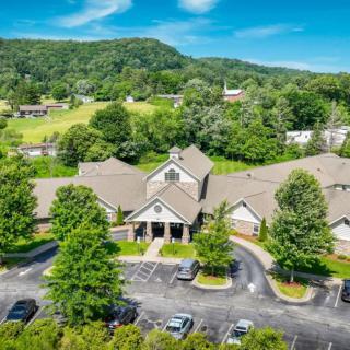 Aerial view of a building surrounded by lush greenery and trees, with a parking lot in the foreground.