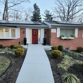 A brick house with a well-maintained front yard and a red door, featuring a concrete pathway leading to the entrance.