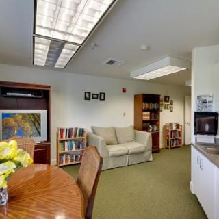 A cozy office space featuring a sofa, bookshelf, table with chairs, and decorative artwork.