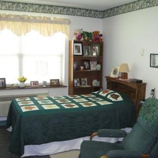 A cozy bedroom with a quilt-covered bed, a bookcase, and a large window.