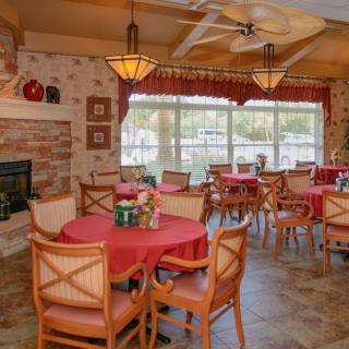 A cozy dining area with multiple tables and chairs, warm lighting, a fireplace, and large windows.