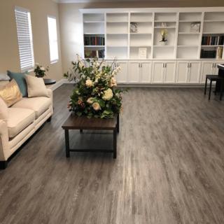 A spacious living room with a beige couch, a table with floral arrangements, and white built-in bookshelves.