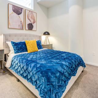 A stylishly decorated bedroom featuring a bed with a blue blanket, yellow accent pillow, and modern artwork on the wall.