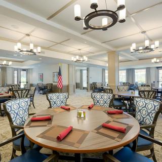 A spacious dining room with neatly arranged tables and chairs, featuring elegant chandeliers and an American flag in the background.