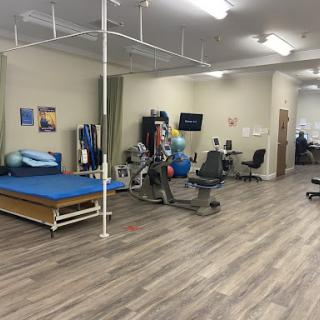A spacious rehabilitation therapy room equipped with exercise equipment and therapy beds.
