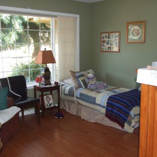A cozy bedroom with a single bed, large window, and wooden flooring.