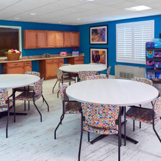 A bright cafeteria with round tables and a kitchen area.