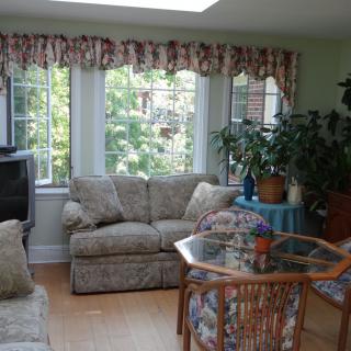 A cozy living room with a sofa, television, and plenty of natural light from large windows and a skylight.
