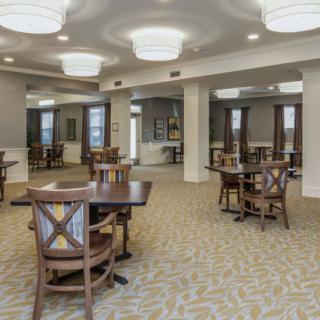 A modern dining area with wooden tables and chairs, elegant lighting, and patterned carpet.