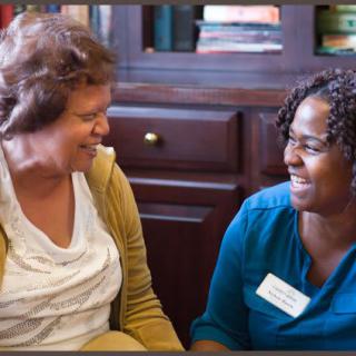Two women smiling and engaging in a conversation indoors.
