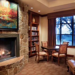 A cozy library nook featuring a stone fireplace, artwork, and a small table with chairs beside a window.