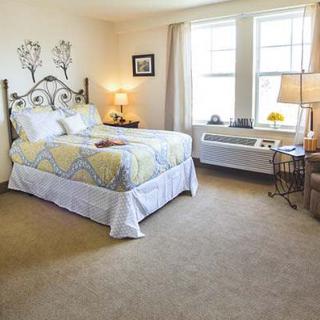 A cozy bedroom with a bed, two lamps, and large windows allowing natural light in.